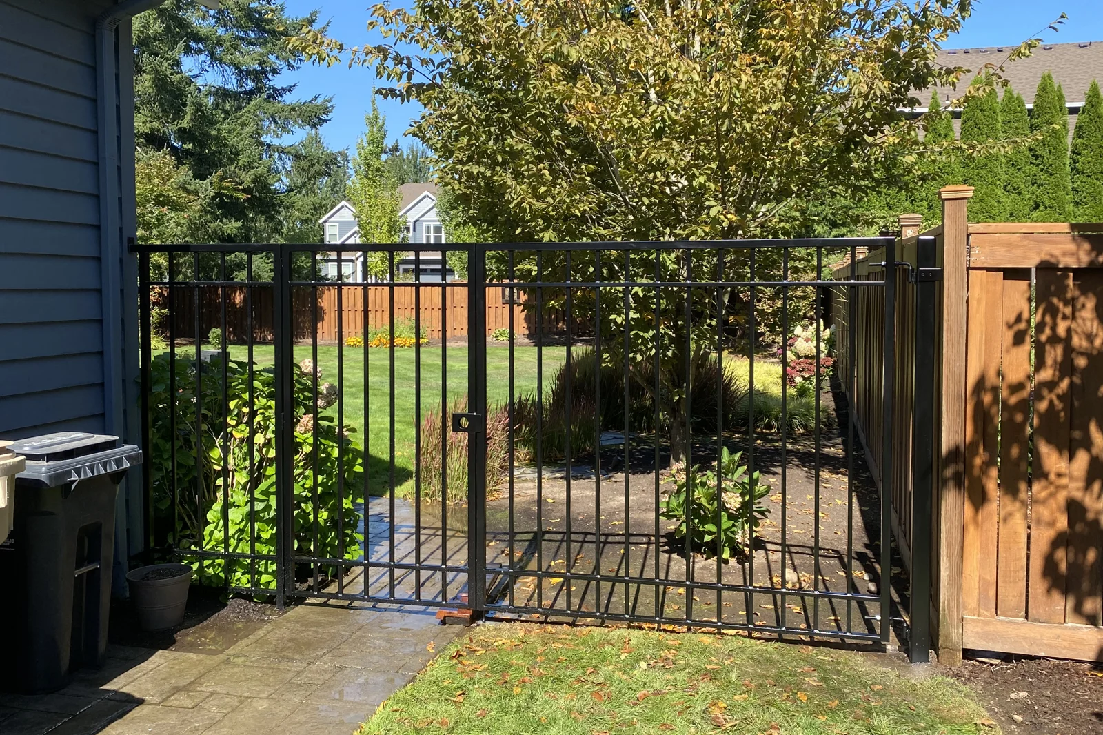 Black flat-top metal pedestrian gate between blue house and cedar fence