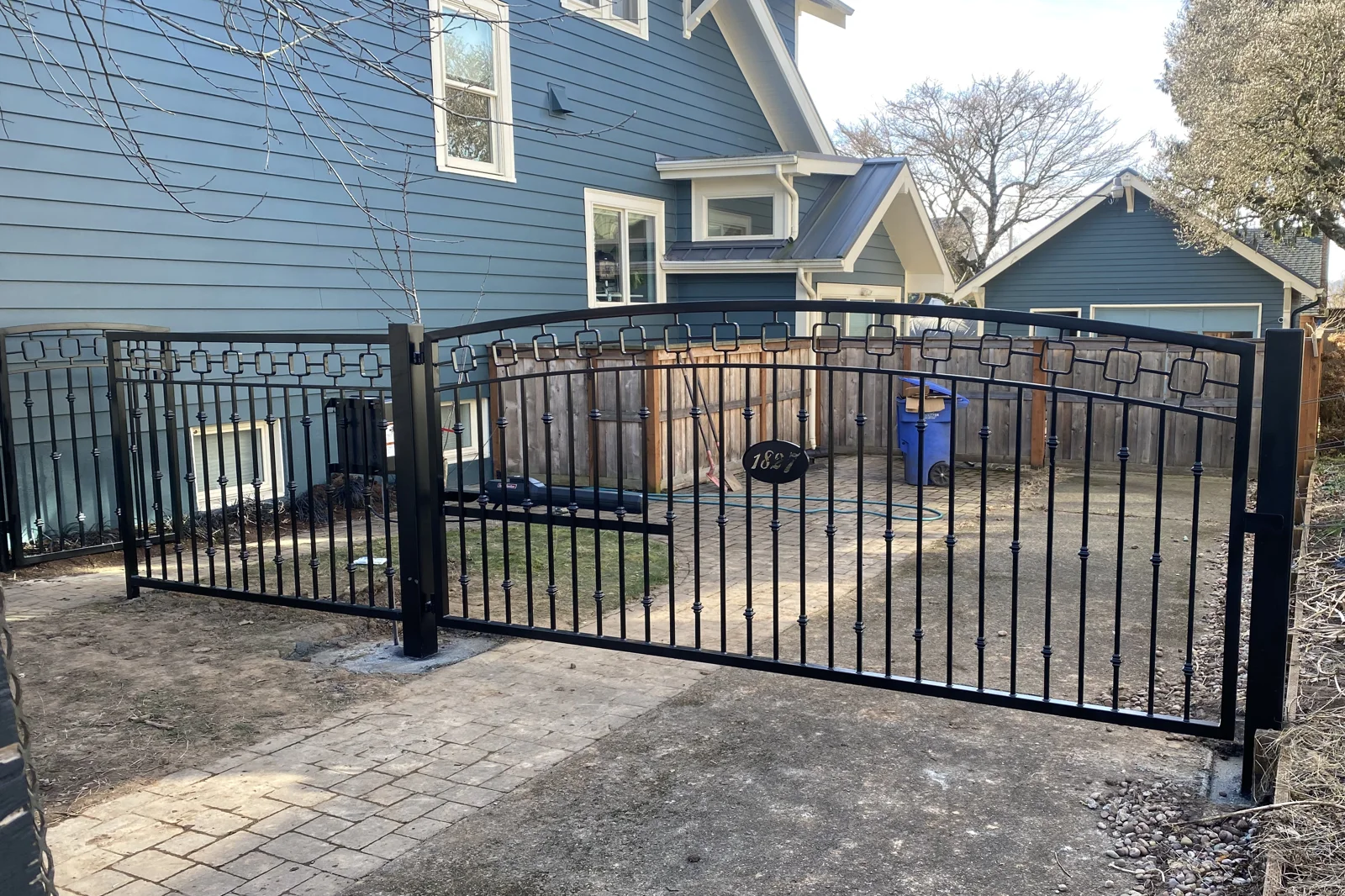 Black wrought iron driveway gate with arched top and square pattern