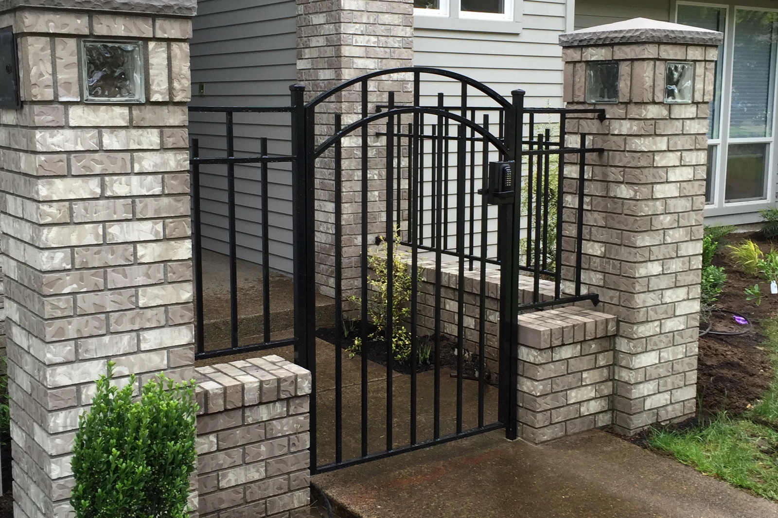 Black arched metal security gate between grey stone pillars