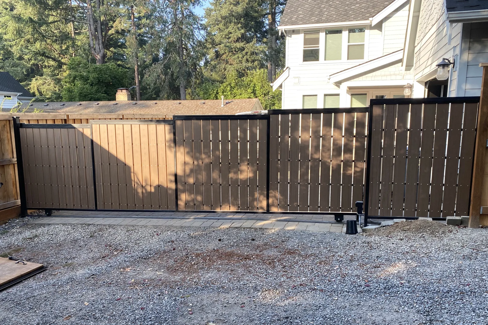 Brown wood-slat sliding driveway gate with black metal frame