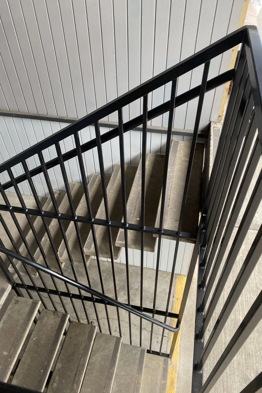 A custom-fabricated black metal commercial stairwell railing with sleek vertical pickets, installed on concrete-filled industrial stairs.