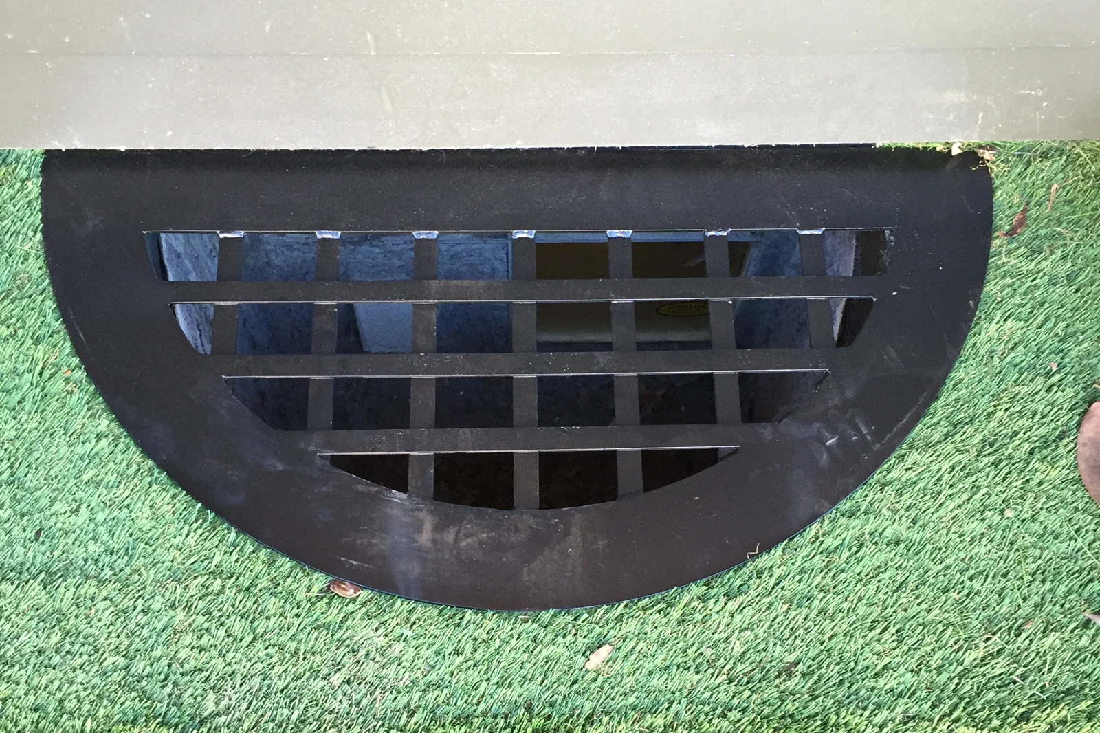 A custom-welded black iron window well grate with a square bar design, installed over a basement window well.