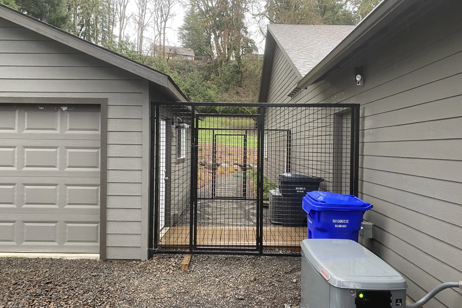 A black custom-welded wire mesh gate with a square steel frame installed between the house and garage, featuring a matching pedestrian gate.