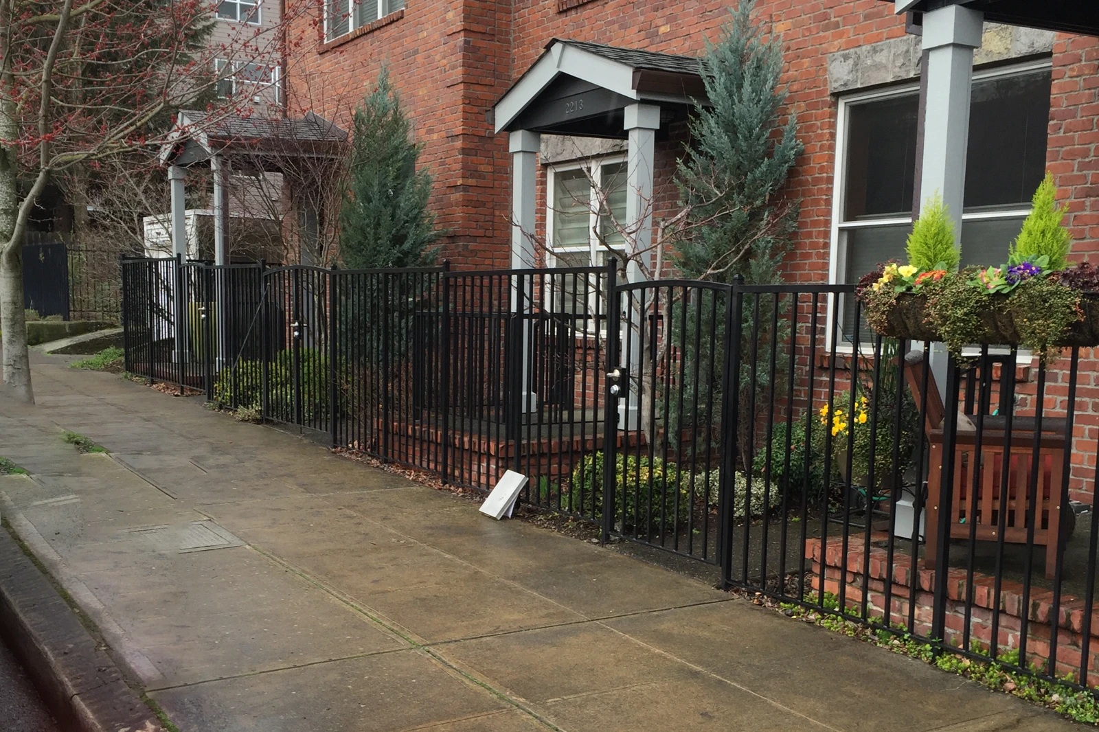 A black ornamental iron picket fence bordering the front yards of red brick townhouses. | Chip and Dale's Iron Works