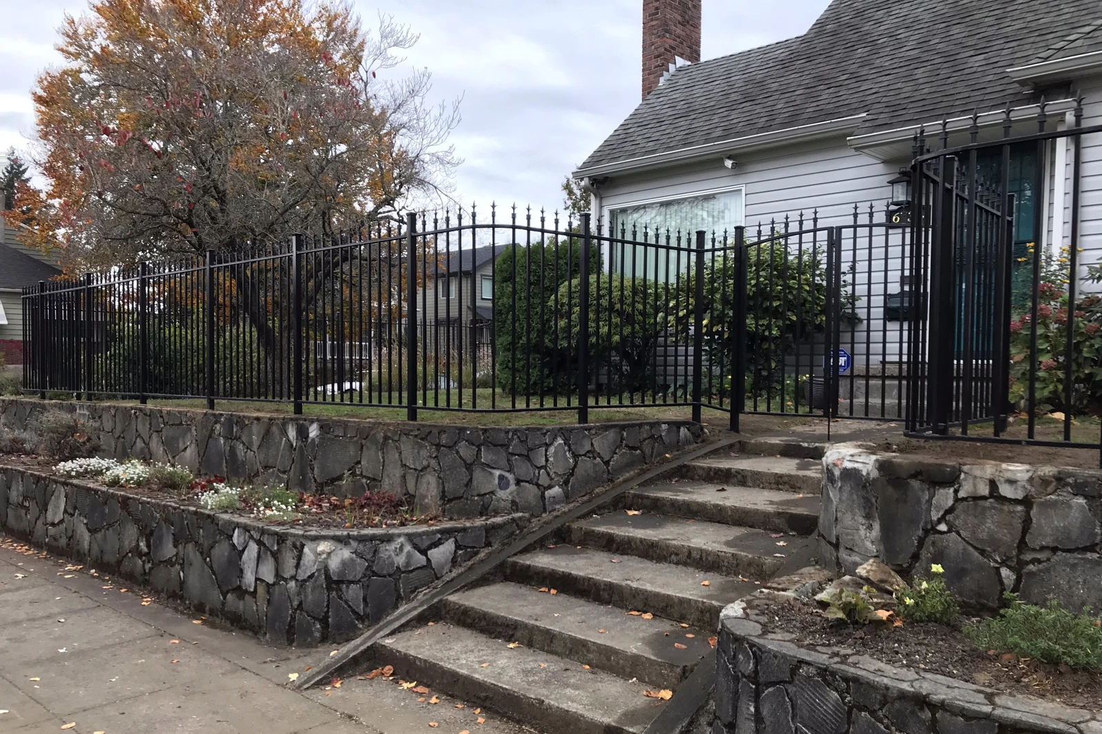A black ornamental iron fence with spear-top finials installed on top of a multi-tiered stone retaining wall.
