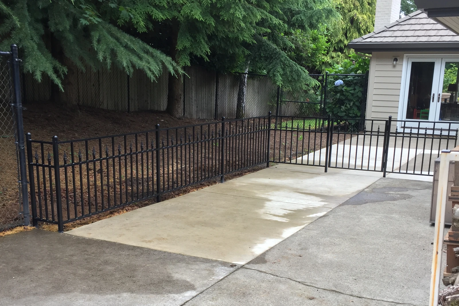 A low-profile black ornamental metal fence with classic spear-top finials and a matching gate, enclosing a concrete patio.