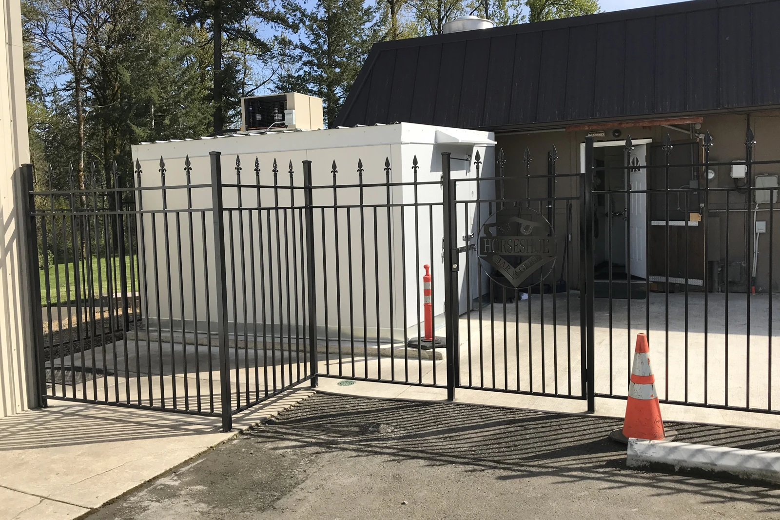 A black ornamental steel security fence with sharp spear-top finials and a matching swinging gate installed around a commercial parking lot. | Chip and Dale's Iron Works