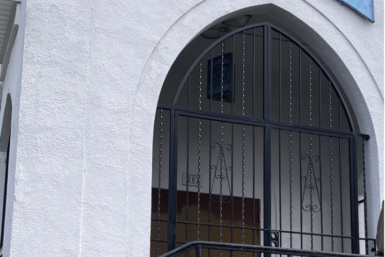 A black wrought iron gothic arch security gate with twisted pickets and decorative scrollwork, in the entryway of a white stucco building.