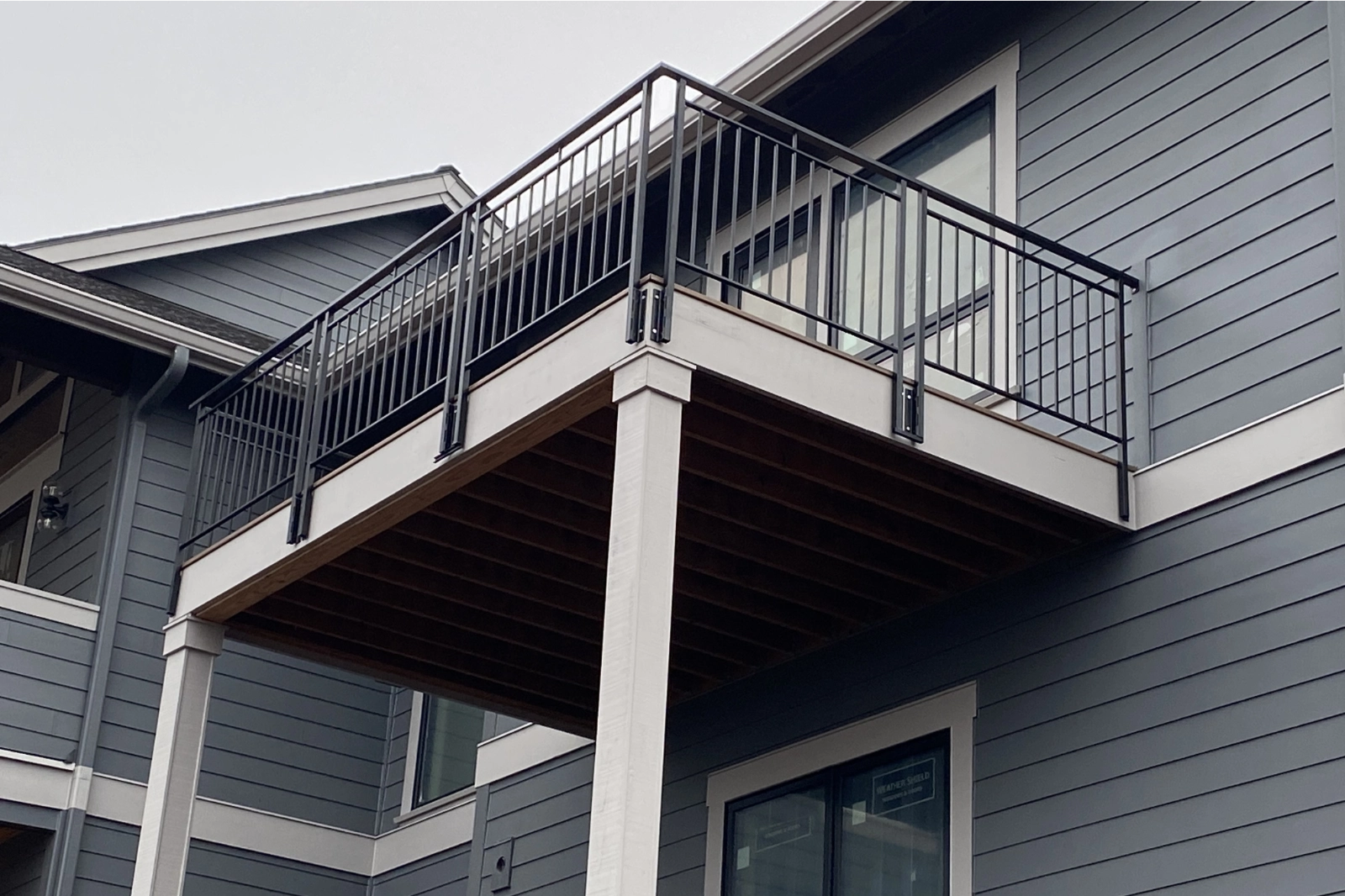 A black steel balcony railing with modern vertical pickets and a matching handrail, securely mounted to an elevated residential deck.