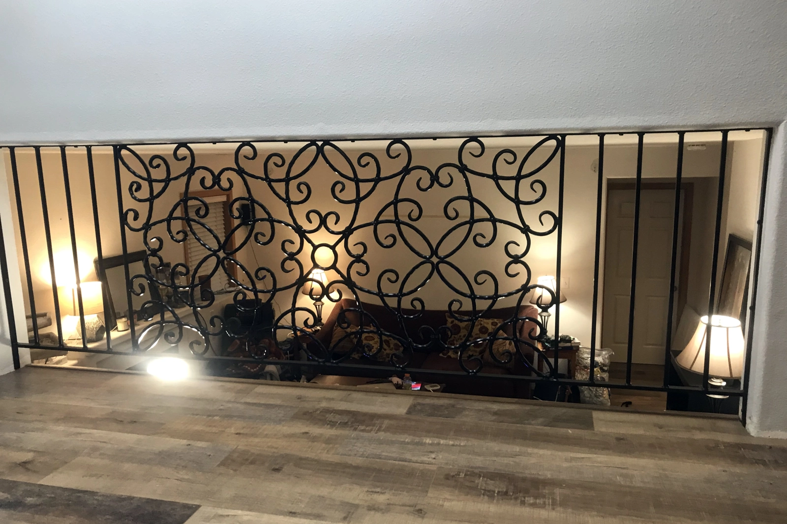 A custom-handcrafted interior mezzanine railing featuring ornate black wrought iron scrollwork panels set between vertical balusters.