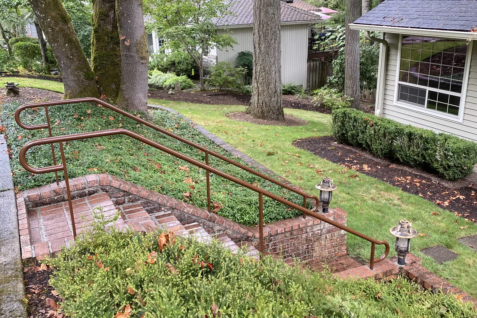 Bronze powder-coated pipe railing with a continuous handrail design, installed on brick outdoor garden stairs.