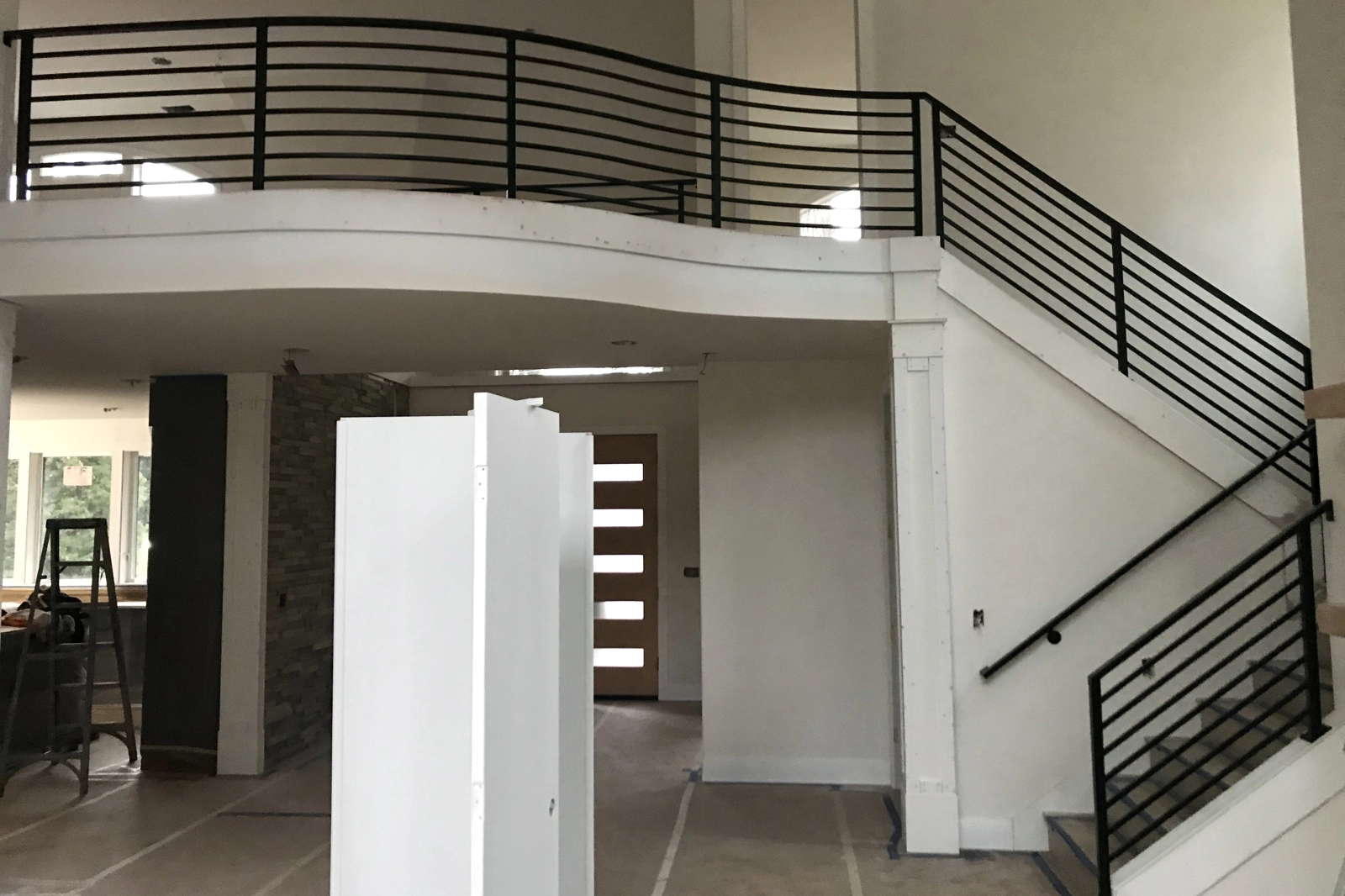 A black metal interior railing system with horizontal bars, installed along a curved residential mezzanine balcony and staircase.