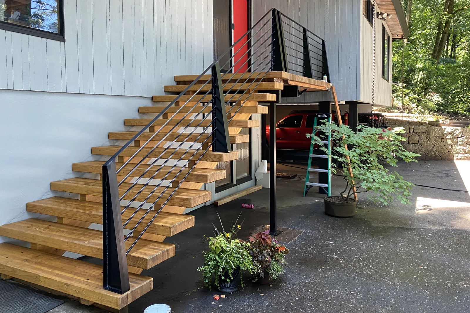 A residential exterior railing system, featuring black metal posts and horizontal rod infill installed on a floating wood staircase and landing.