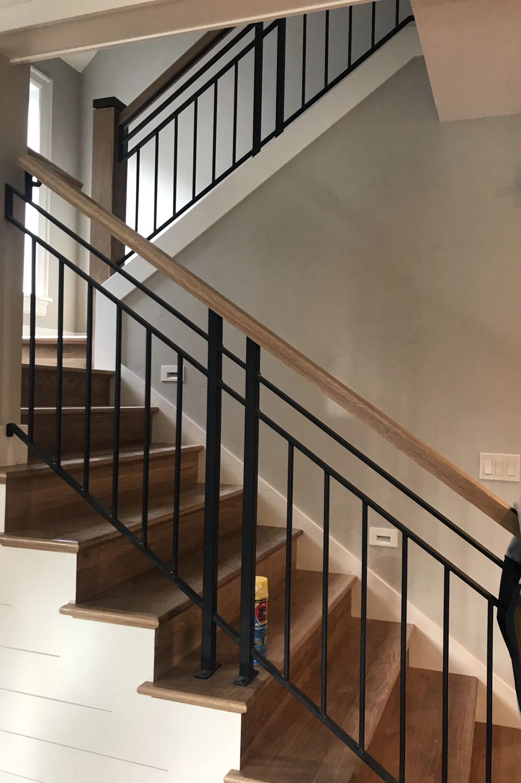 A residential interior staircase featuring black metal railings with vertical balusters and warm natural wood handrails.