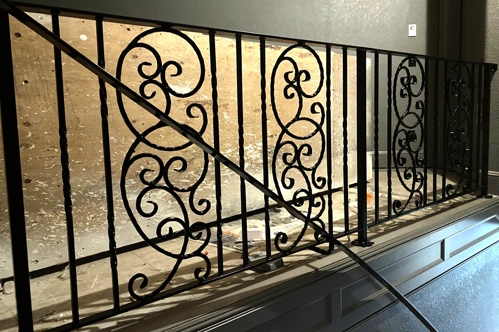 A custom residential interior railing system featuring black wrought iron with ornate decorative scrollwork panels and twisted metal pickets.