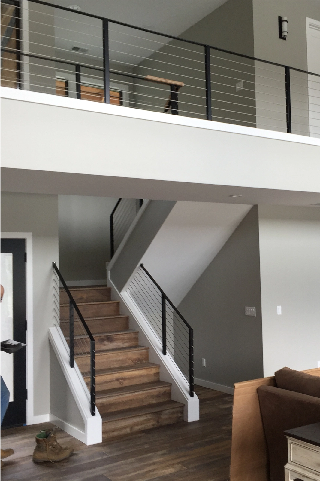 A residential interior railing, featuring black steel posts and horizontal cable infill on a hardwood staircase and matching upstairs balcony.