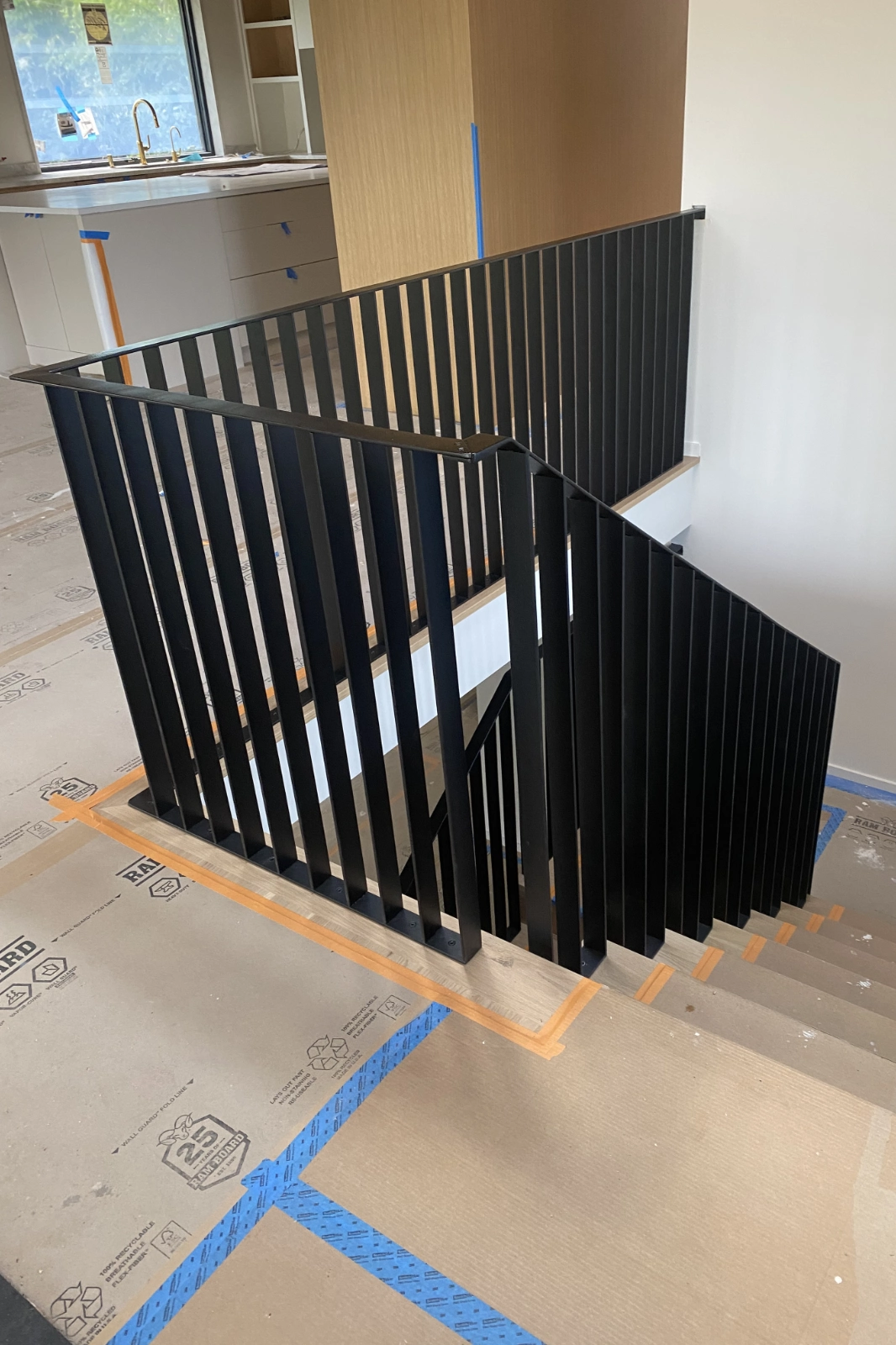 A residential interior staircase featuring a modern matte black vertical flat bar railing system and matching handrail.