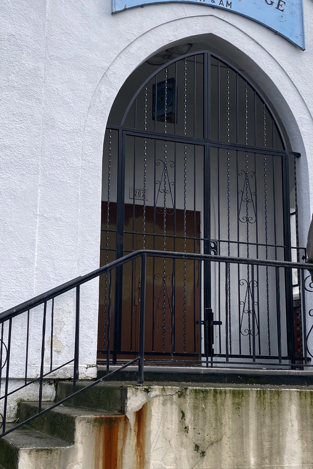 A black wrought iron gothic arch security gate with twisted pickets and decorative scrollwork, in the entryway of a white stucco building.