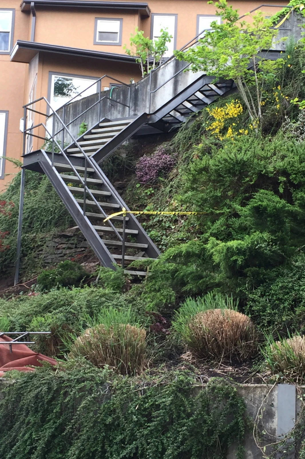 A custom-fabricated industrial metal staircase zig-zagging down a steep, lushly landscaped hillside with sleek modern railings and durable open treads.