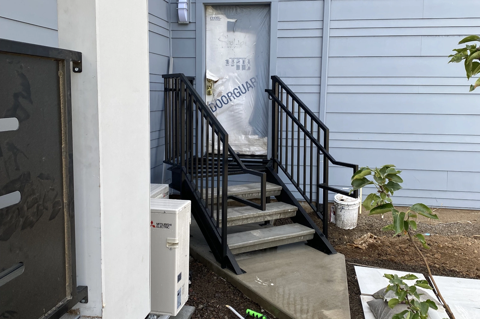 A custom-fabricated black metal entry staircase with industrial concrete treads and matching picket railings leading to a modern home entrance.