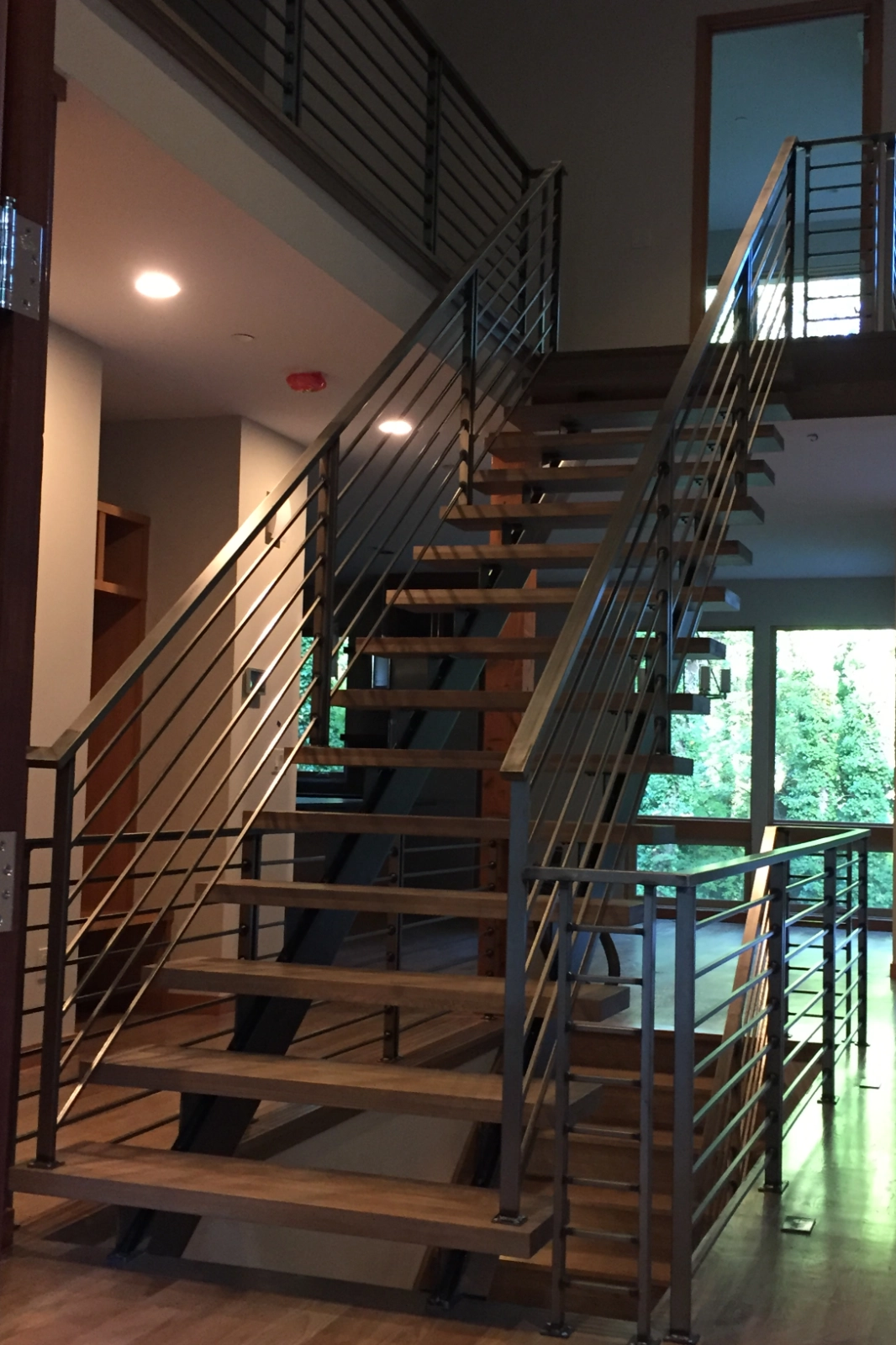 A high-end custom interior staircase featuring thick wooden floating treads, a central steel stringer, and a modern stainless steel horizontal cable railing system.